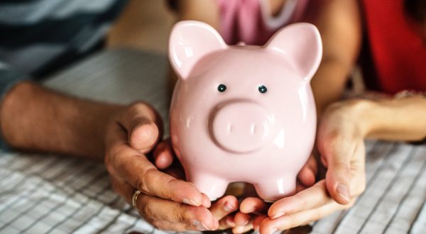 Close up of family's hands holding piggy bank with coins spilled out around them.